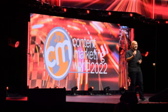 Light skinned black man wearing a black shirt and black pants on stage. Content Marketing World 2022 on screen in the background.