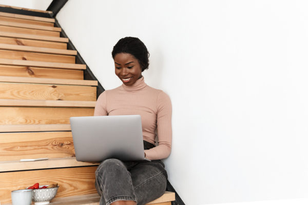 Black woman sitting on wood stairs with a laptop in her lap.